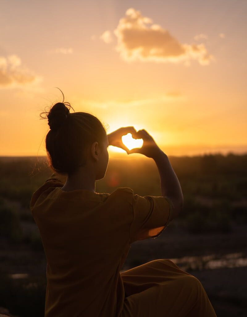 Silhouette of a person forming a heart with hands against a Morocco sunset.