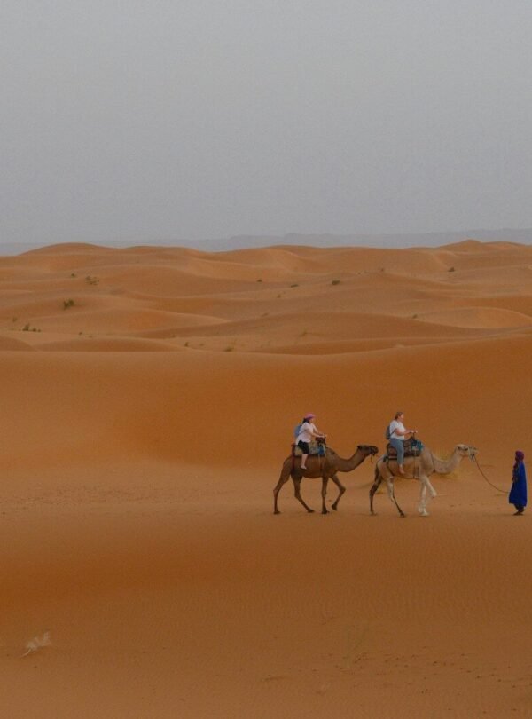 Two people riding camels in a vast desert landscape.